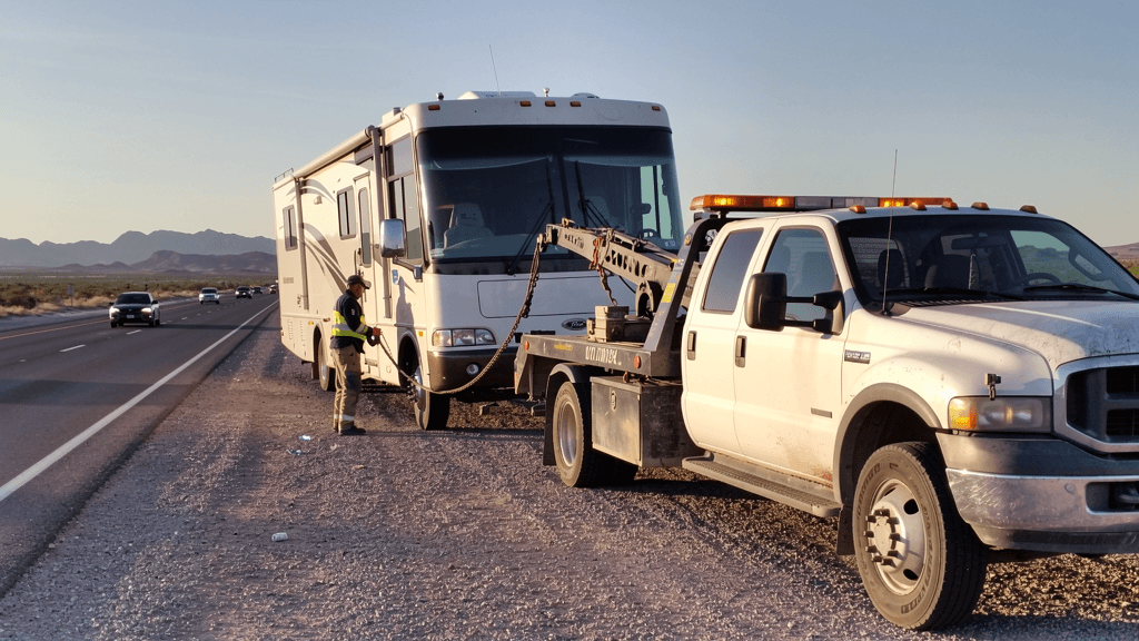 Tow truck assisting a motorhome on a desert highway shoulder