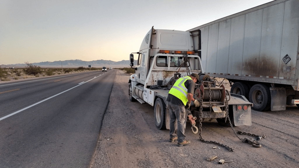 Tow operator setting up for a semi-truck tow near an industrial road